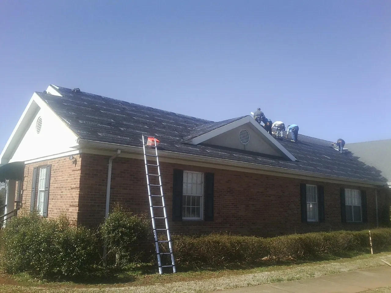 Crew tearing shingles off a brick ranch roof with a ladder set — Emergency Roof Repair work by our crew in Califon