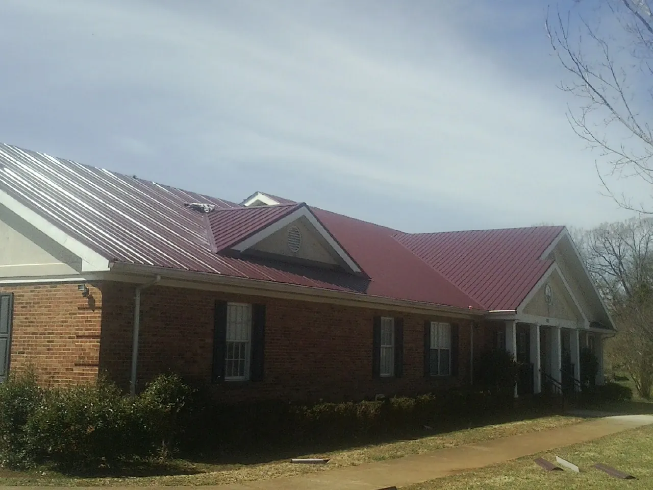 Red metal roof with gabled entries on a long brick building, from a Hail Damage Roof Repair job in Califon