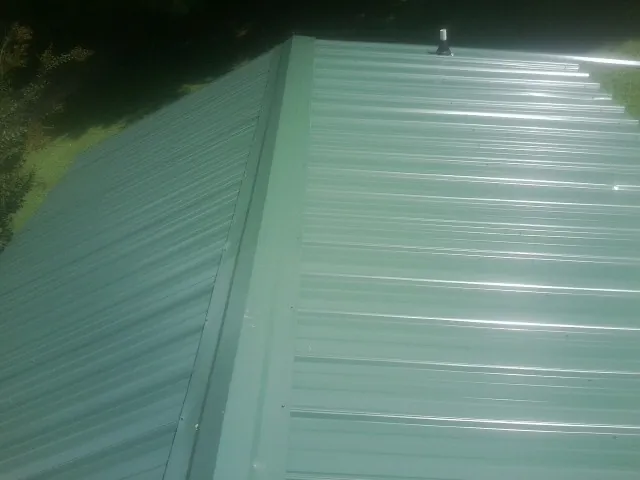New green metal panels meeting at the ridge of a roof — Flat Roof Repair work by our crew in Califon