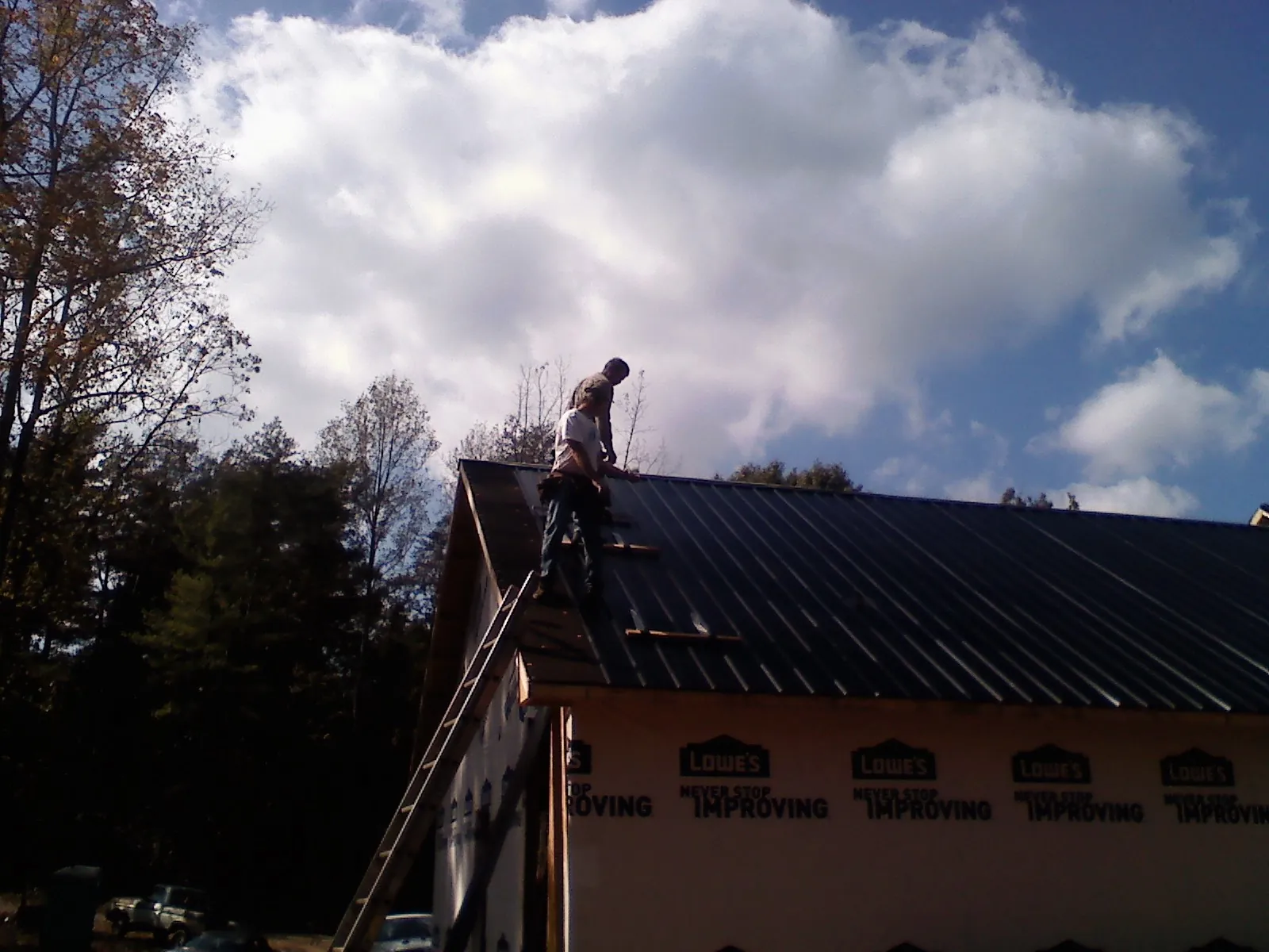 Roofer fastening dark metal panels high against a cloudy sky, from a Roof Inspection job in Califon