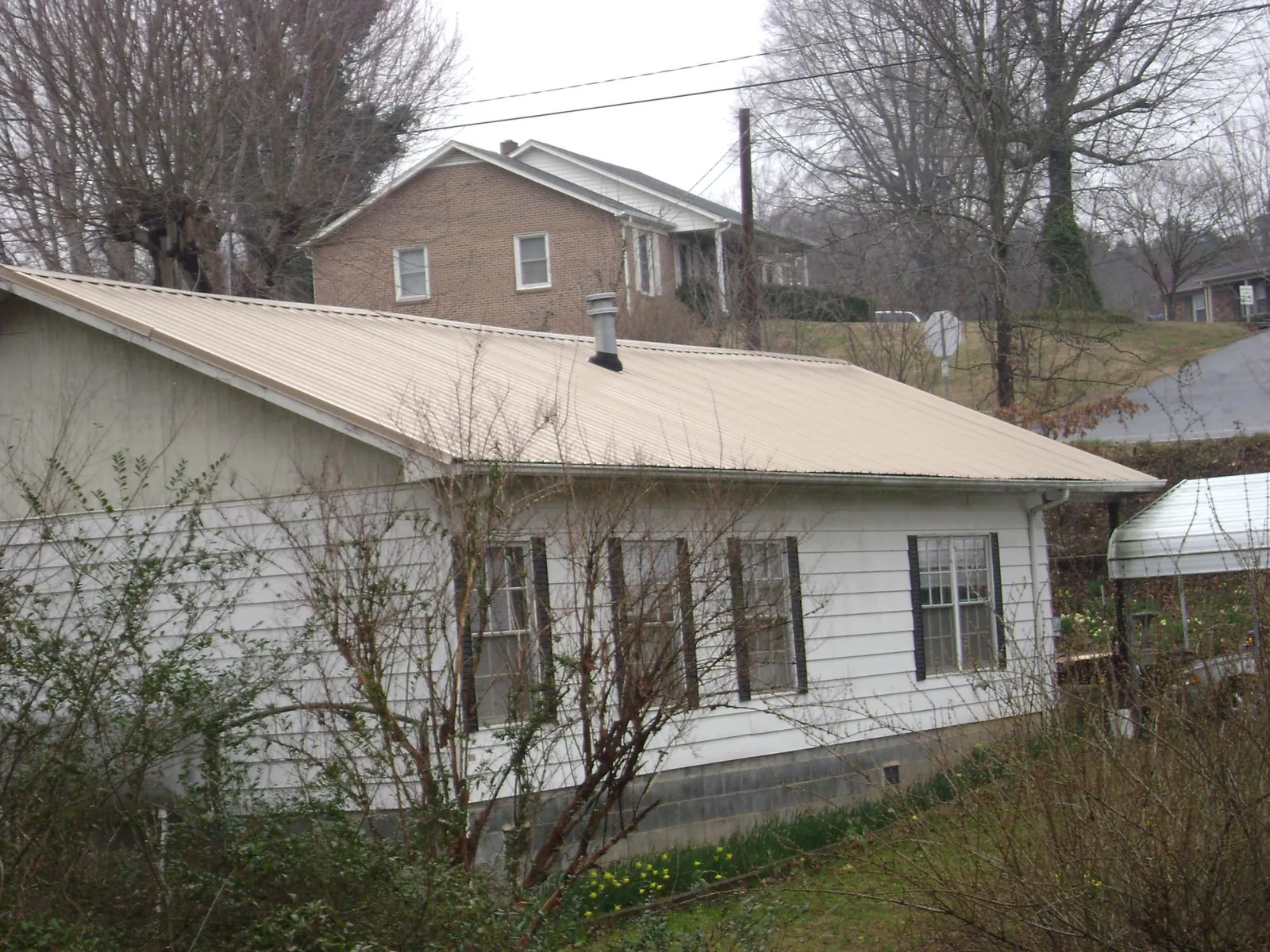 Tan metal roof on a white sided house set into a hillside — Commercial Roofing by Roofing Brothers in Califon